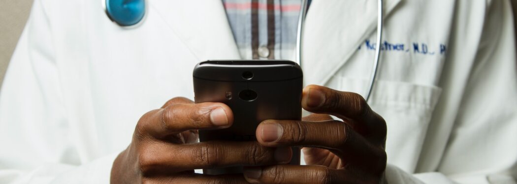 person wearing lavatory gown with green stethoscope on neck using phone while standing