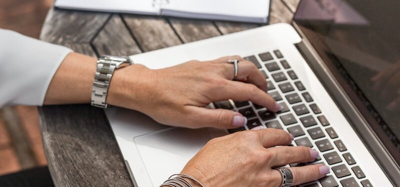 person typing on MacBook Pro on brown wooden table during daytime photo