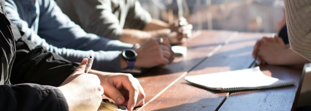 people sitting on chair in front of table while holding pens during daytime